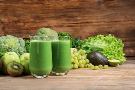 Glasses of fresh green smoothie and ingredients on wooden table, space for textの写真素材