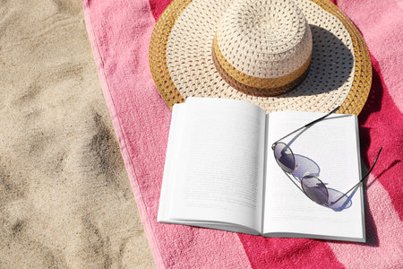 Open book, sunglasses, hat and striped towel on sandy beach, above view. Space for textの写真素材