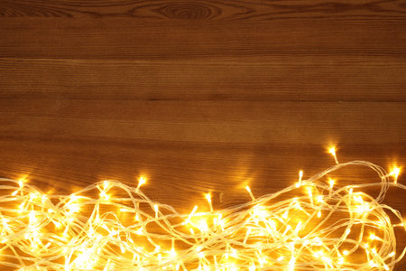 Beautiful glowing Christmas lights on wooden table, top view. Space for text