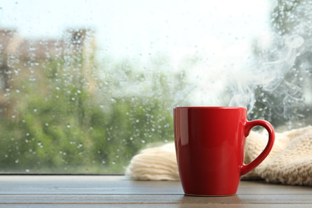 Cup of hot drink and knitted plaid near window on rainy day. Space for textの写真素材