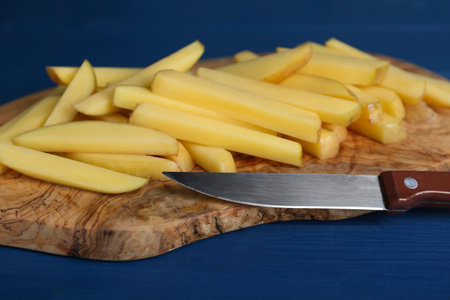 Cut raw potatoes and knife on blue wooden table, closeup. Cooking delicious French friesの写真素材