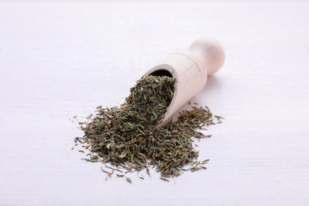 Scoop with dried thyme on white wooden table, closeup