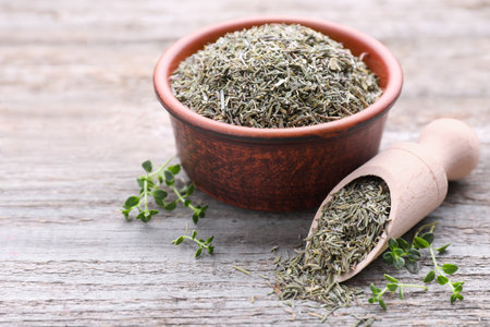 Bowl with scoop of dried and fresh thyme on wooden table, closeup