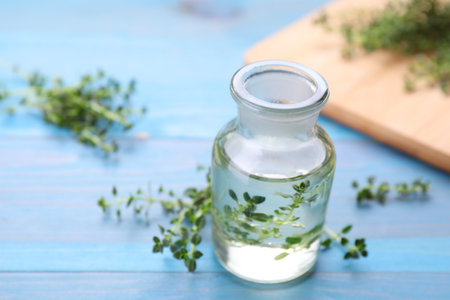 Bottle of thyme essential oil and fresh plant on light blue wooden table, closeup. Space for textの写真素材