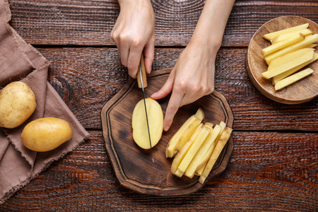 Woman cut potatoes on wooden table, top viewの写真素材