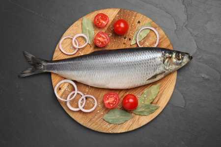 Tray with salted herring, onion rings, bay leaves and cherry tomatoes on black table, top viewの写真素材
