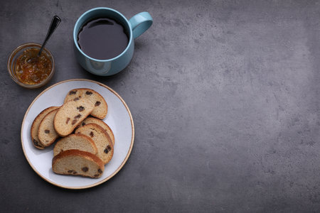 Sweet hard chuck crackers with raisins, jam and cup of tea on gray table, flat lay. Space for text