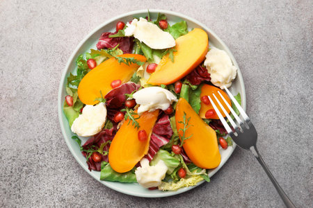 Delicious persimmon salad with cheese and pomegranate served on gray table, top viewの写真素材