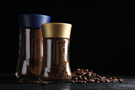 Glass jars with aromatic instant and ground coffee near beans on black wooden table. Space for textの写真素材
