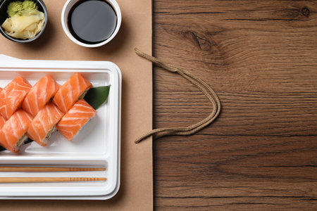 food delivery. Delicious sushi rolls served on wooden table, flat lay with space for textの写真素材