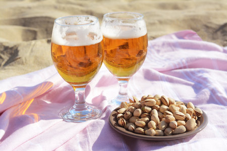 Glasses of cold beer and pistachios on sandy beachの写真素材