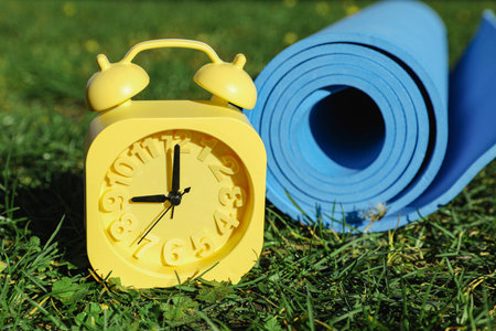 Alarm clock and fitness mat on green grass outdoors, closeup. morning exerciseの写真素材