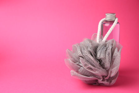 Gray shower puff and bottle of cosmetic product on pink background, space for textの写真素材