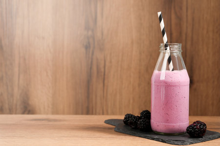 Delicious blackberry smoothie in glass bottle with straw and fresh berries on wooden table. Space for textの写真素材