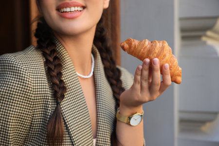 Smiling woman holding tasty croissant outdoors, closeupの写真素材
