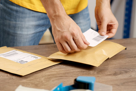 Post office worker sticking barcode on parcel at counter indoors, closeupの写真素材