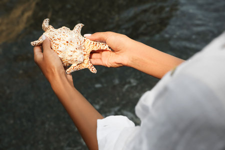 Young woman holding beautiful big seashell outdoors, closeupの写真素材