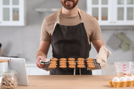 Man holding grid with freshly baked cookies in kitchen, closeup. Online cooking coursesの写真素材