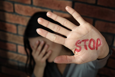 domestic violence concept. Unhappy woman near brick wall, focus on hand with written word Stopの写真素材