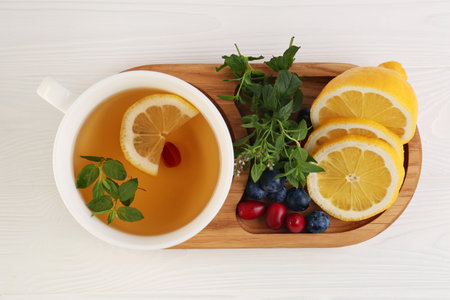 Cup with delicious immunity boosting tea and ingredients on white wooden table, top view