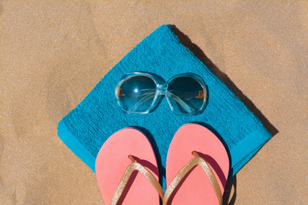 Folded soft blue beach towel with flip flops and sunglasses on sand, flat layの写真素材