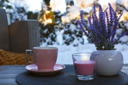 Burning candle, potted flowers and cup of hot drink on coffee table outdoors. Cozy winterの写真素材