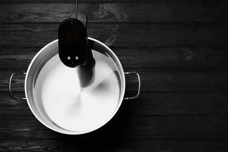 Thermal immersion circulator in pot on black wooden table, top view with space for text. Sous vide cookerの写真素材