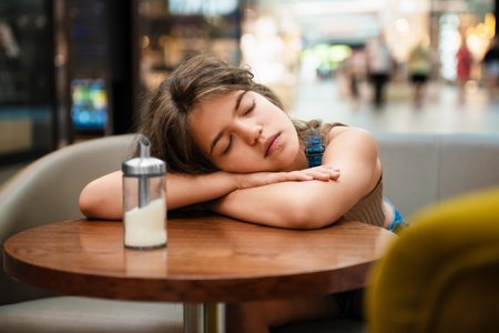 Tired teenage girl sleeping on wooden table in cafeの写真素材