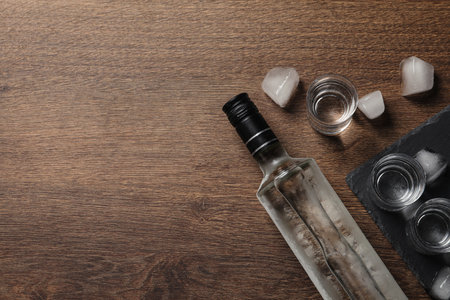 Bottle of vodka, shot glasses and ice cubes on wooden table, flat lay. Space for textの写真素材
