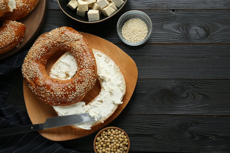Delicious bagel with tofu cream cheese and soy beans on black wooden table, flat lay. Space for text