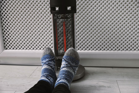 Man warming feet near modern heater indoors, closeup