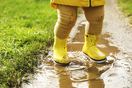 Little girl wearing rubber boots walking in puddle, closeup