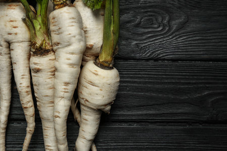 Tasty fresh ripe parsnips on black wooden table, flat lay. Space for text