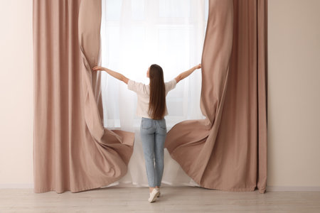 Woman opening stylish curtains at home, back viewの写真素材