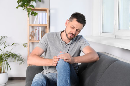 Man suffering from knee pain on sofa at homeの写真素材