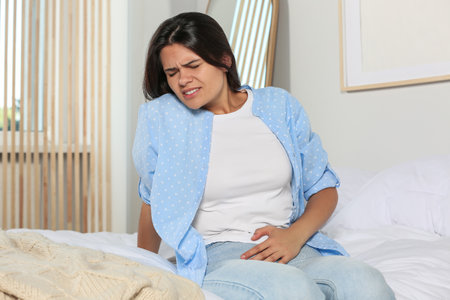 Young woman suffering from cystitis on bed at homeの写真素材