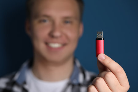Man with usb flash drive against blue background, focus on device. Space for textの写真素材