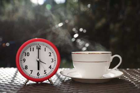 Alarm clock and cup with hot drink on tableの写真素材
