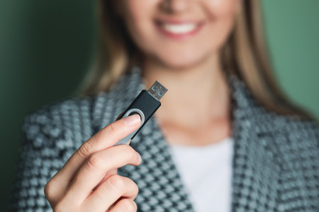 Woman holding usb flash drive against green background, focus on hand