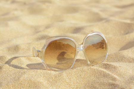 Stylish sunglasses with light brown lenses on sandy beach, closeupの写真素材