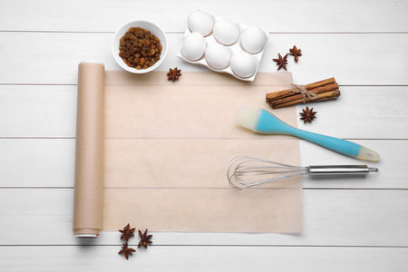 Baking parchment paper and different ingredients on white wooden table, flat lay. Space for text