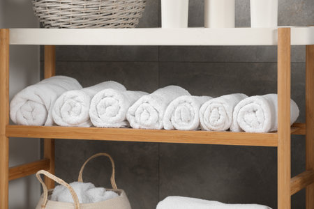 Wooden shelf and wicker basket with soft terry towels in bathroom