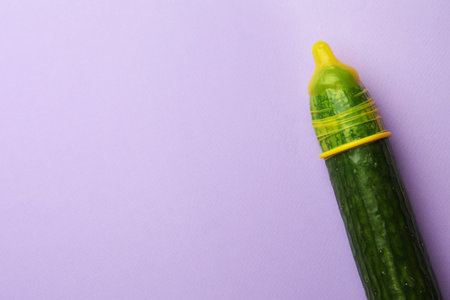 Cucumber with condom on lilac background, top view and space for text. Safe sex conceptの写真素材