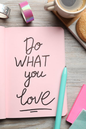 Open notebook with motivational phrase Do What You Love on wooden table, flat layの写真素材
