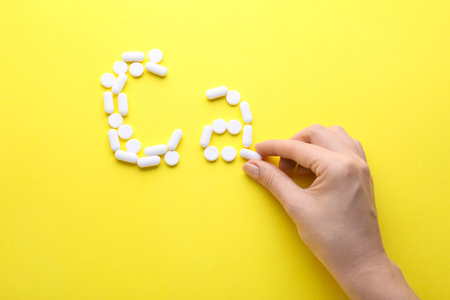 Woman making calcium symbol with white pills on yellow background, top viewの写真素材