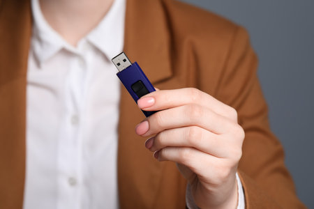 Woman holding usb flash drive against gray background, focus on hand
