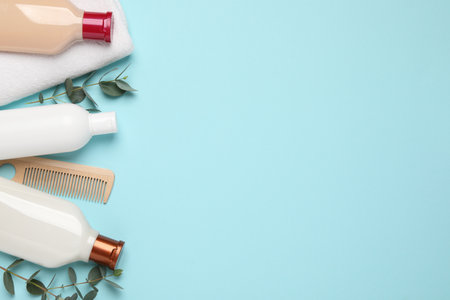 Shampoo bottles, wooden comb, towel and leaves on turquoise background, flat lay. Space for textの写真素材