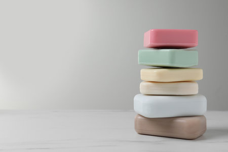 Stack of different soap bars on white marble table. Space for text