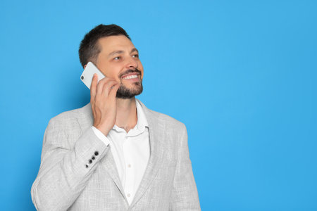 Handsome man talking on phone against light blue background. Space for textの写真素材