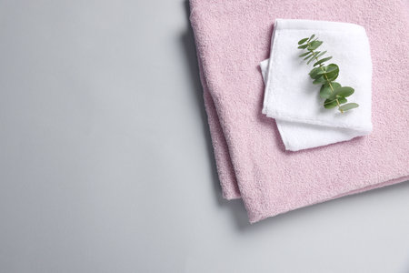 Soft folded towels with eucalyptus branch on light gray background, top view. Space for textの写真素材